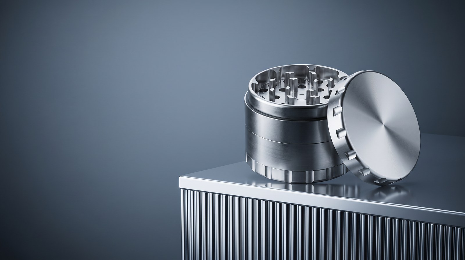 Geöffneter Edelstahl Grinder mit angelehntem Deckel auf einem Metallsockel vor blaugrauem Hintergrund